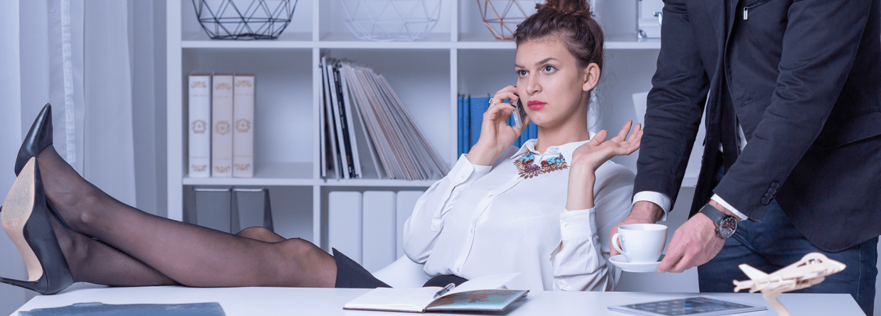 Vrouwelijke ondernemer achter haar bureau met haar voeten op tafel krijgt een kopje koffie van werknemer